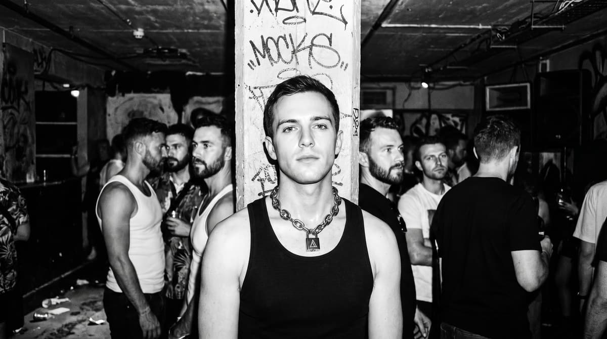 KI-generiertes Motiv: Junger Mann mit schwerer Halskette im Kellerclub, dahinter die Crowd